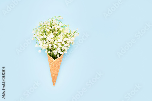Lily-of-the-valley bouquet in waffle ice cream cone on a blue background