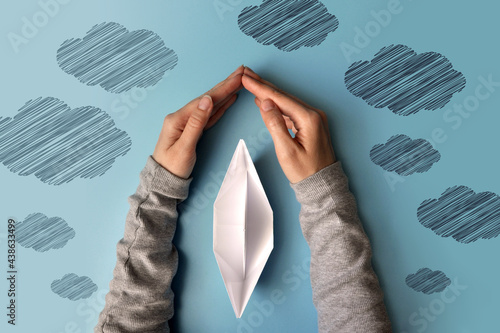 Hands protect the paper boat from bad weather. A symbol of protection of life and an easy way in life