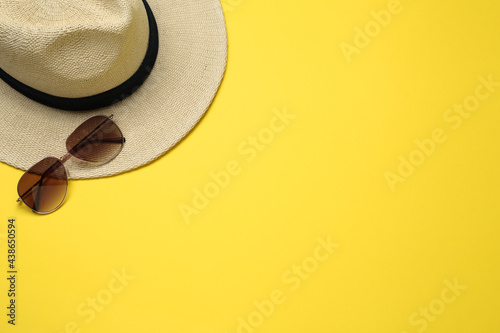 Hat and sunglasses on yellow background, flat lay with space for text. Sun protection