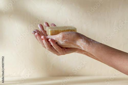 natural cosmetics, hygiene and beauty concept - foamy hands holding bar of craft soap on beige background