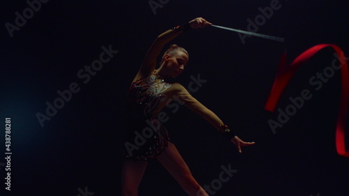 Beautiful gymnast performing sports equipment. Girl doing exercises with ribbon.