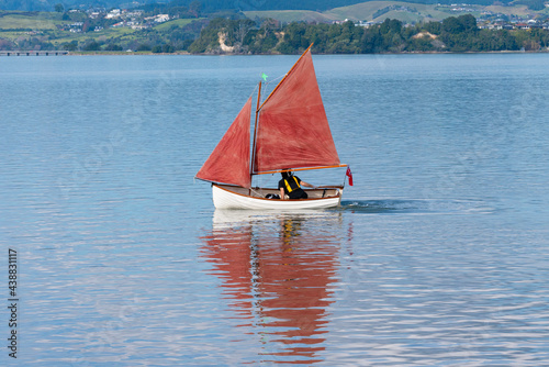 Traditional style red sails on small yacht becalmed in bay.