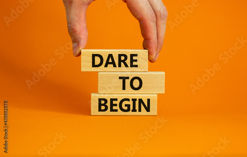 Dare to begin symbol. Wooden blocks with words 'Dare to begin'. Beautiful orange background, businessman hand. Business, dare to begin concept, copy space.