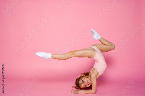 Cute little girl workout in a leotard on a pink background. Space for text.