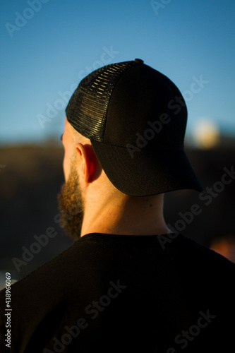Crea tu mock up. Imagen urbana de un chico con gorra y barba de espaldas en la hora dorada. Fotografía de producto. Espacio para texto sobre fondo natural