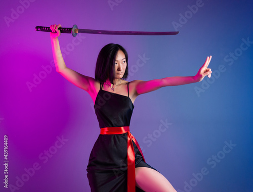slender Asian woman in a black dress with a katana in her hand image of a samurai on a neon background