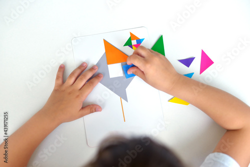 A preschooler girl sitting at the table collects a drawing from a geometric figure. the concept of early childhood development by montessori. a game of logic and imagination.