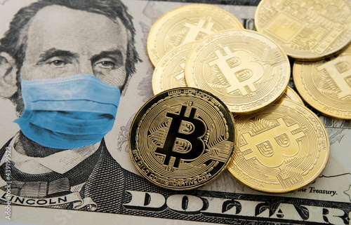 Cryptocurrency regulation in the United States after COVID-19 pandemic. Concept. Picture of Bitcoin coins placed on 5 dollars note with applied anti virus face mask (digital montage).