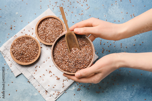 Female hands with bowl of flax seeds on color background