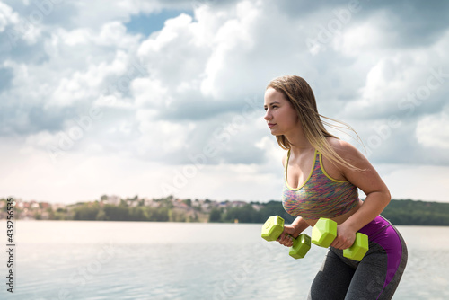 Young fitness athletic trener doing exercises with dumbbells on beach lake.