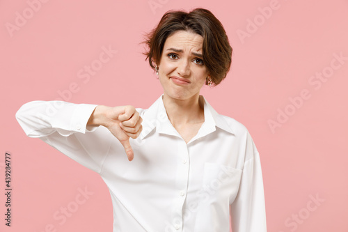 Young displeased dissatisfied employee business woman corporate lawyer in classic formal white shirt work in office showing thumb down dislike gesture isolated on pastel pink color background studio.