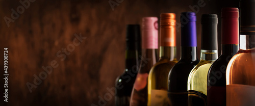 Wine bottles collection row in wine cellar, winery basement, bar or shop on dark wooden background