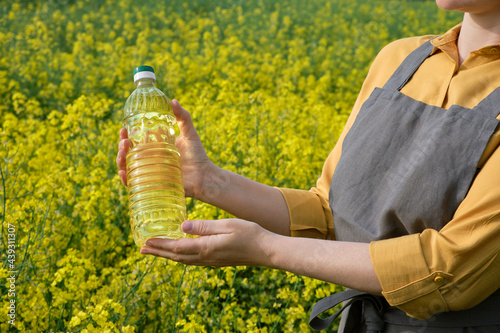 A woman stands in a rape field and holds a bottle of rapeseed oil in his hands. Concept of canola oil production.