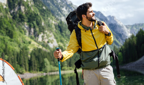Hiker young man with backpack and trekking poles looking at the mountains in outdoor