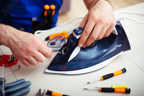 Close up photo of concentrated young man while he is fixing damaged iron on his workplace with tools