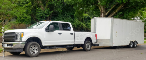 White pickup truck and large utility trailer parked on residential city street.