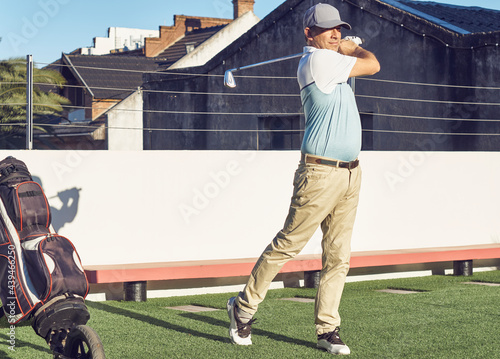 Hombre practicando swing de golf, con su carro y palos