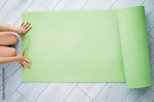 Kids home fitness. Training indoors. Active lifestyle. Health wellbeing. Unrecognizable girl hands on unrolled green yoga mat on light floor with copy space.