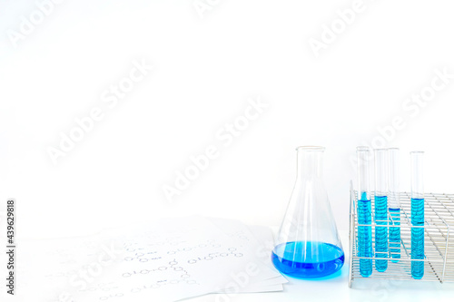 白背景に着色された溶液の入ったフラスコと試験管、テーブルに置かれた分子構造の資料