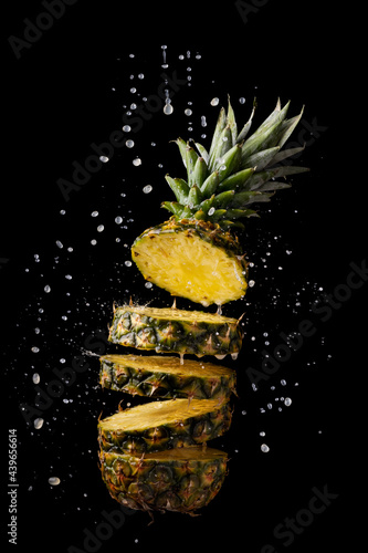 fresh and sliced pineapple with juice splashes on black background