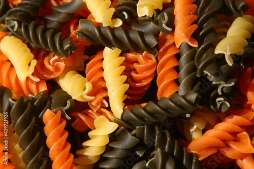 Three Colors Rotini Pasta. Pasta fusilli tricolore background. Abstract texture of colorful pasta. Pattern of macaroni. Bright multicolor food backdrop. Uncooked colored noodles.