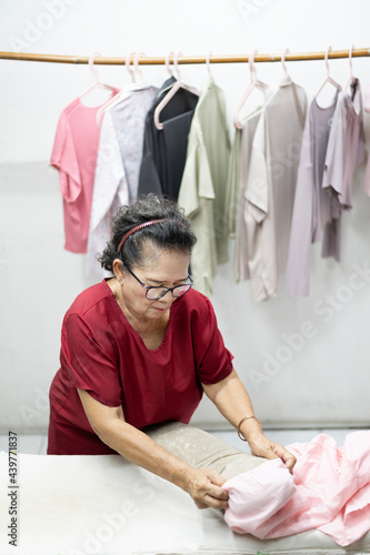 An Asian elderly woman who is a housewife folding clothes at the laundry shop.