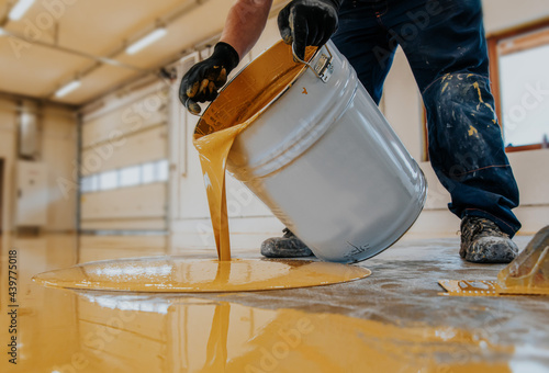 Closeup shot of a construction worker pouring out epoxy resin from a bucket onto a floor