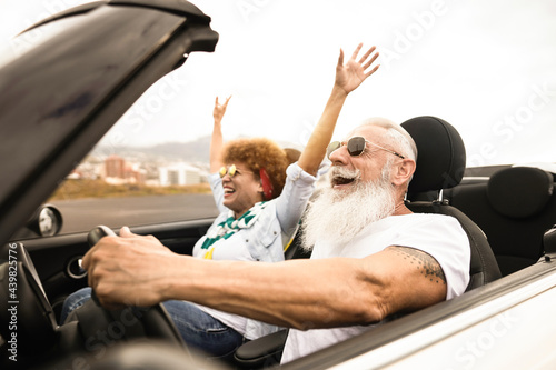 Happy senior couple having fun in convertible car during summer vacation - Focus on man face