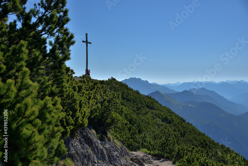 Das Gipfelkreuz auf dem Herzogstand mit Blick über die Silhouetten von Berggipfel