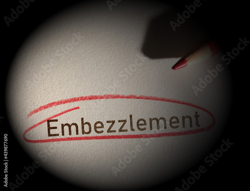 Embezzlement text circled in red pencil on dark background