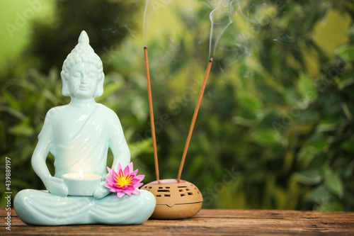Buddha statue with burning candle and lotus flower near incense sticks on wooden table. Space for text