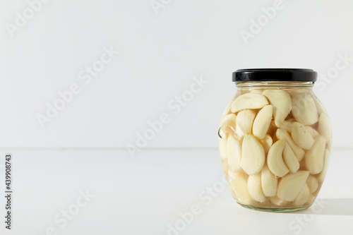 Pickled garlic in jar. Glass jar with preserved garlic on white background with copy space.