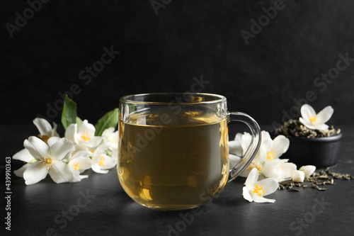 Glass cup of jasmine tea and fresh flowers on black table
