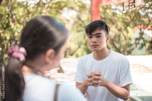 A young asian male begging for forgiveness from his girlfriend. Relationship issues in teenagers. Outdoor noon scene.