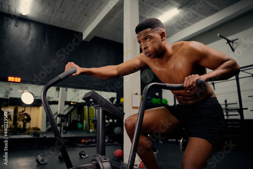 African American male using an elliptical trainer during cross fit training. Male athlete exercising intensely in the gym. High quality photo