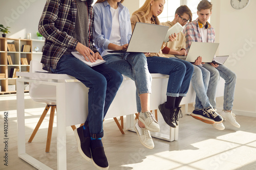 Middle section teenager secondary or high school student studying using laptop and paper copy-book, notebook sitting on classroom desk. Teen pupils involved in learning process working together