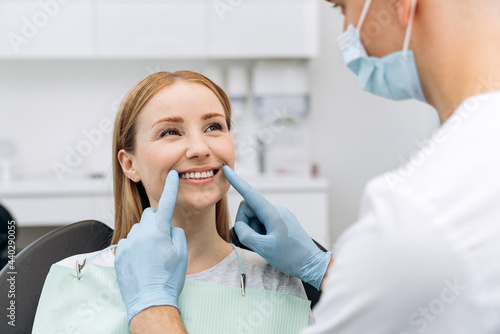 Dentist checks the teeth of an attractive woman. The doctor in rubber gloves touches the patient's teeth