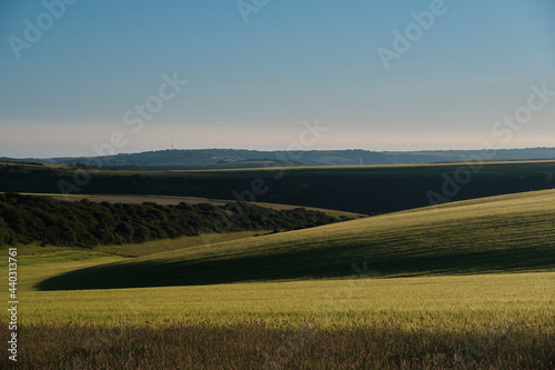 Farmland on a sunny evening in the South Downs National Park with the sun setting over the Sussex Weald. Newhaven and wind turbines in the far distance. 