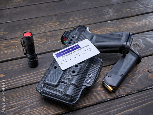 Concealed Carry Permit laying on handgun in holster with spare magazine and hand light