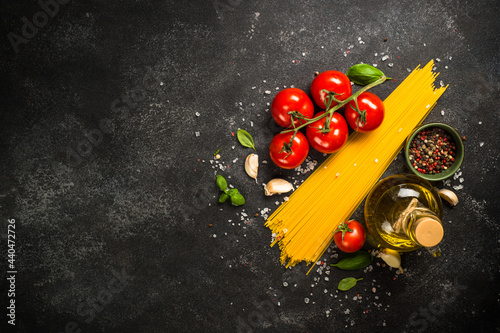 Italian food background at black table. Pasta, olive oil, spices, basil and fresh tomatoes. Top view with copy space.