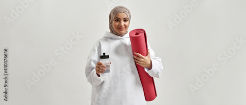 Happy young arabian woman in hijab holding sport mat