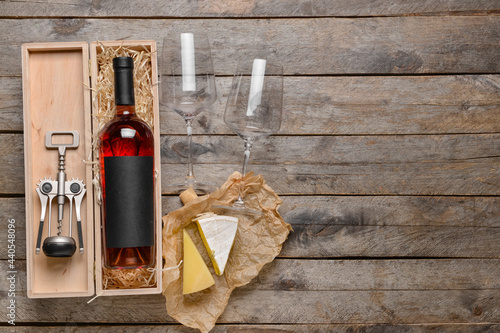 Box with bottle of wine, cheese and glasses on wooden background