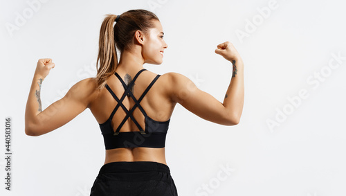 Sport and women. Rear view of strong fitness athlete, female bodybuilder, flexing muscles, showing fit body, biceps and athletic back, smiling satisfied, white background