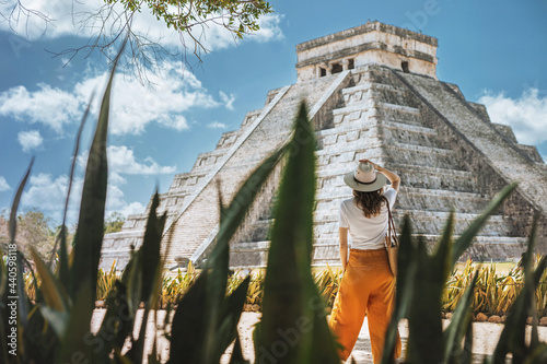 A young woman tourist in a hat stands against the background of the pyramid of Kukulcan in the ancient Mexican city of Chichen Itza. Travel concept.Mayan pyramids in Yucatan, Mexico