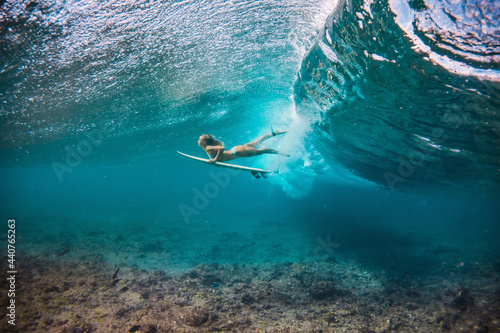 beautiful woman in the bikini doing duck dive with the surfboard under the breaking waves in the clear water of the Indian Ocean 