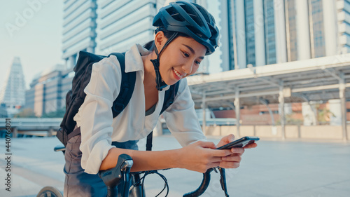 Smile asian businesswoman with backpack use smart phone look camera in city stand at street with bike go to work at office. Sport girl use phone for work. Commute to work, Business commuter in city.