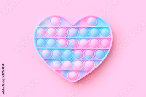 Colorful antistress sensory toy fidget push pop it in shape of heart on pink background, top view