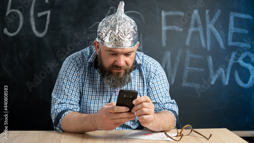 portrait of a crazy conspiracy theorist with a mobile phone in his hands and a protective cap made of foil is of electric waves and radiation. Conspiracy theory and the Internet user.