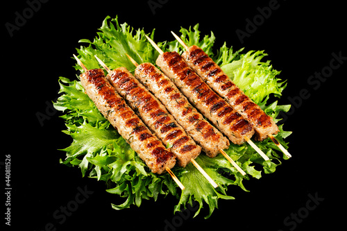 Chevapchichi, meat appetizer on a black background. Lettuce leaves complement the meat dish. Lula-Kebab. Selective focus.