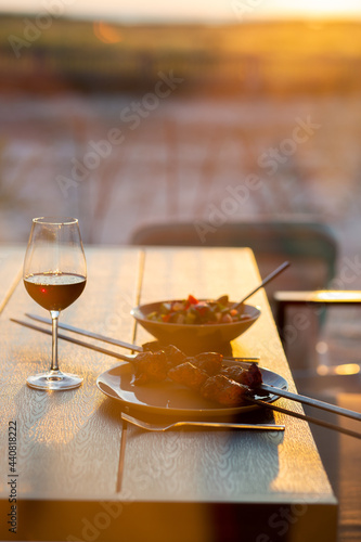 A glass of wine with grilled meat on the summer terrace.A glass of wine at sunset with dinner in the summer.Picnic.Dinner on the street with wine.Meat on a skewer with salad.Mediterranean diet.Summer 